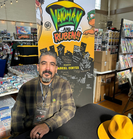 Photo of Gabriel Cortes the creator of VATOMAN …and RUBEN!! Sitting at table during March 2025 Salinas Toy Show event